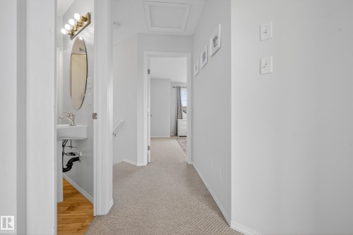 Hallway featuring light gray walls, carpeted flooring, and a view into a room with light-colored furniture and a window - 9051 Scott Crescent, Edmonton, AB - Indoor Photo Showing Other Room