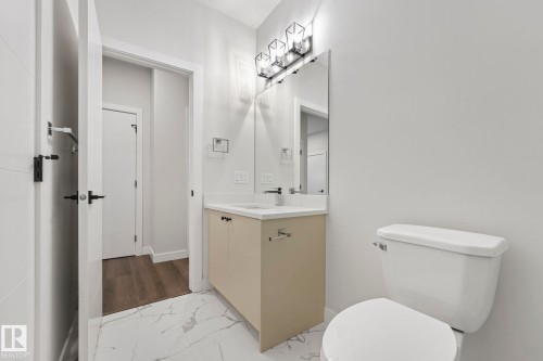 Bathroom featuring a white toilet, a vanity with a light-colored countertop and dark faucet, a mirror, and a modern light fixture - 14 Dalquist Bay, Leduc, AB - Indoor Photo Showing Bathroom
