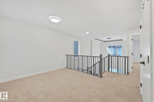 Well-lit interior space featuring light-colored carpet, white walls, and a staircase with a dark railing - 14 Dalquist Bay, Leduc, AB - Indoor Photo Showing Other Room