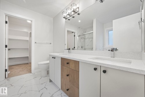 Bathroom featuring a double vanity with white countertops, modern light fixtures, and a spacious walk-in closet with shelving - 14 Dalquist Bay, Leduc, AB - Indoor Photo Showing Bathroom