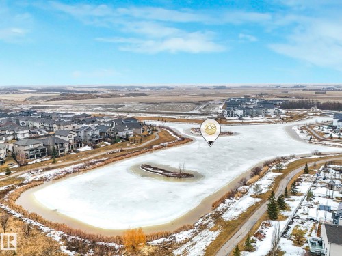 Aerial view showcasing the property's location within a residential area, overlooking a frozen pond with an island, and surrounded by pathways - 14 Dalquist Bay, Leduc, AB - Outdoor With View