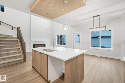 Open concept interior featuring light wood flooring, a central island with a sink, and a fireplace - 14 Dalquist Bay, Leduc, AB - Indoor Photo Showing Kitchen With Double Sink