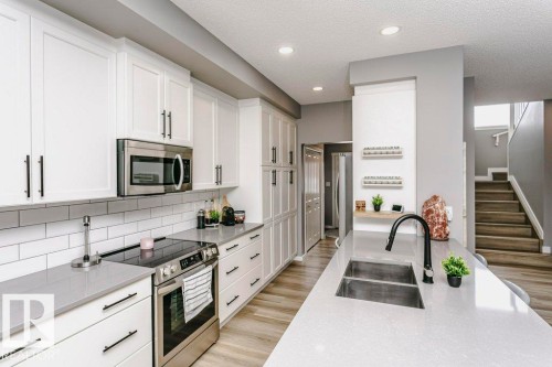The kitchen features white cabinetry with dark hardware, stainless steel appliances, and light-colored countertops - 320 Balsam Link, Leduc, AB - Indoor Photo Showing Kitchen With Upgraded Kitchen