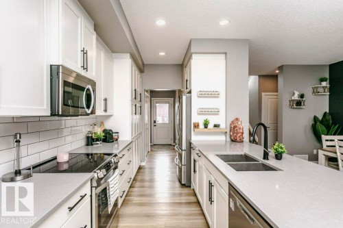 The kitchen features white cabinetry with black hardware, light-colored countertops, and stainless steel appliances including an oven, microwave, and dishwasher - 320 Balsam Link, Leduc, AB - Indoor Photo Showing Kitchen With Double Sink With Upgraded Kitchen