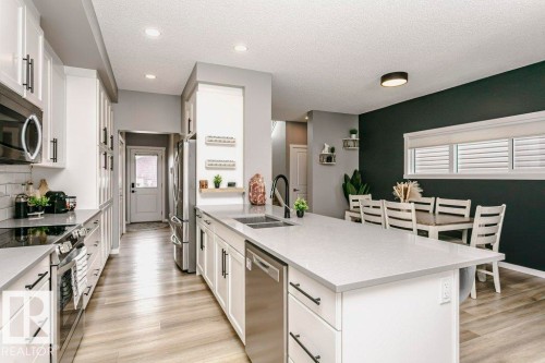The kitchen features white cabinetry with black hardware, stainless steel appliances, and light-colored countertops - 320 Balsam Link, Leduc, AB - Indoor Photo Showing Kitchen With Double Sink With Upgraded Kitchen