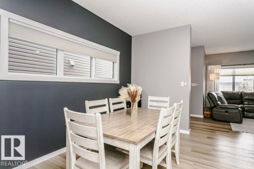 The dining area features a light wood table with seating for six, complemented by a prominent window with horizontal blinds and a roller shade - 320 Balsam Link, Leduc, AB - Indoor Photo Showing Dining Room