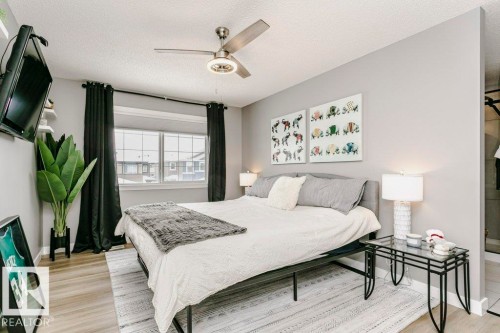 This bedroom features light-colored walls, a ceiling fan with integrated lighting, and a large window with dark curtains - 320 Balsam Link, Leduc, AB - Indoor Photo Showing Bedroom
