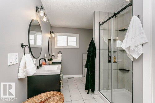 Bathroom featuring a double vanity with dark cabinetry, modern black fixtures, and circular mirrors - 320 Balsam Link, Leduc, AB - Indoor Photo Showing Bathroom