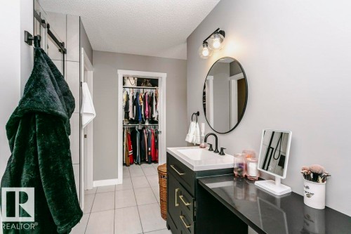 This space features a vanity with a white countertop and a black faucet, complemented by an oval mirror and modern wall sconces - 320 Balsam Link, Leduc, AB - Indoor