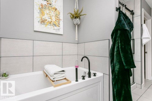 Bathroom featuring a white bathtub with a black faucet, and light-colored tiled walls - 320 Balsam Link, Leduc, AB - Indoor Photo Showing Bathroom
