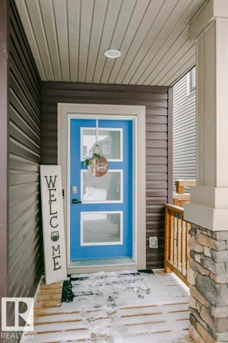 The property features a bright blue front door with three window panels, framed by siding and a stone-clad pillar - 320 Balsam Link, Leduc, AB - Outdoor With Exterior