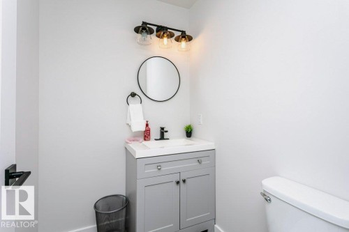 Bathroom featuring a vanity with a white countertop and gray cabinetry, a wall-mounted circular mirror, and a three-light fixture with glass shades - 320 Balsam Link, Leduc, AB - Indoor Photo Showing Bathroom