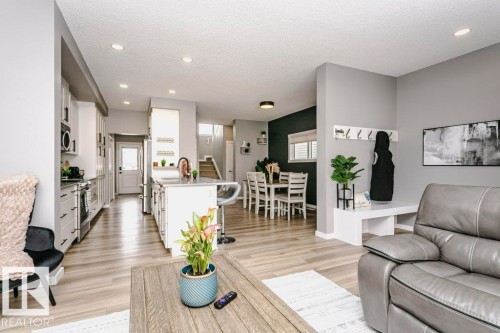 The open-concept living space features light wood-style flooring, recessed lighting, and a kitchen with white cabinetry and stainless steel appliances - 320 Balsam Link, Leduc, AB - Indoor Photo Showing Living Room