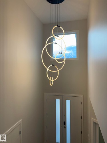 Entryway featuring a multi-tiered circular chandelier, double entry doors with frosted glass panels, a square window, and light-toned wall finishes - 1039 151 Ave, Edmonton, AB 