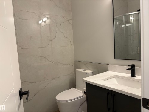 Contemporary bathroom featuring a dark vanity with a white countertop and integrated sink, matte black faucet, rectangular mirror, and light-toned, large-format tile walls - 1039 151 Ave, Edmonton, AB 