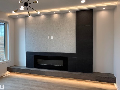 Contemporary fireplace feature wall with a linear electric fireplace, grey tile surround, black tile accents, and a wide floating wood-finish hearth - 1039 151 Ave, Edmonton, AB 