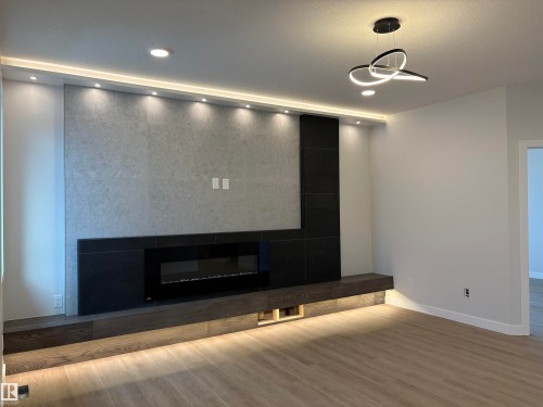 Feature wall with an integrated electric fireplace, accented by recessed lighting and a wood-finish mantel - 1039 151 Ave, Edmonton, AB 