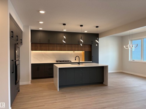 Modern kitchen featuring dark cabinetry with matte black hardware, a light-toned countertop, and an integrated oven and microwave - 1039 151 Ave, Edmonton, AB 