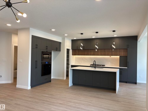 Modern kitchen featuring dark cabinetry, a spacious island with a white countertop, and integrated appliances - 1039 151 Ave, Edmonton, AB 