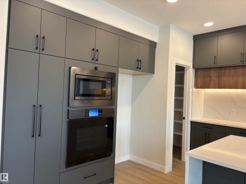 Contemporary kitchen featuring floor-to-ceiling gray cabinetry, integrated stainless steel microwave, and built-in oven - 1039 151 Ave, Edmonton, AB 