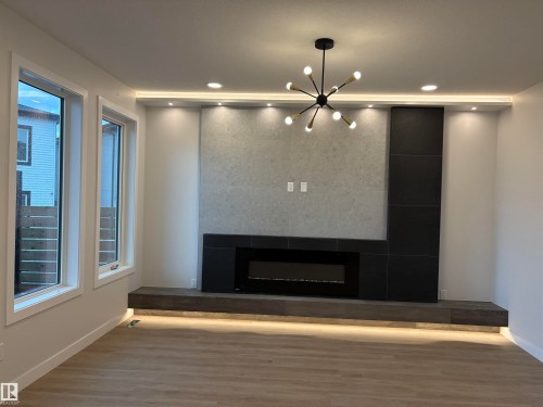 Modern living space featuring a linear electric fireplace, recessed lighting, and a contemporary sputnik chandelier - 1039 151 Ave, Edmonton, AB 