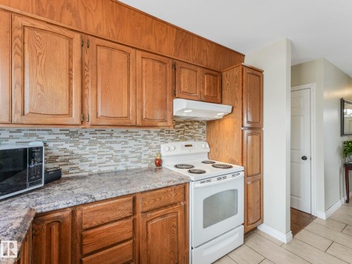 The kitchen features wood cabinetry, a tiled backsplash, and stone-look countertops - 16106 79A Avenue Nw, Edmonton, AB - Indoor Photo Showing Kitchen