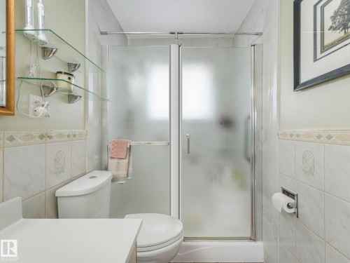 The bathroom features a toilet, a shower with frosted glass doors, and tiled walls - 16106 79A Avenue Nw, Edmonton, AB - Indoor Photo Showing Bathroom