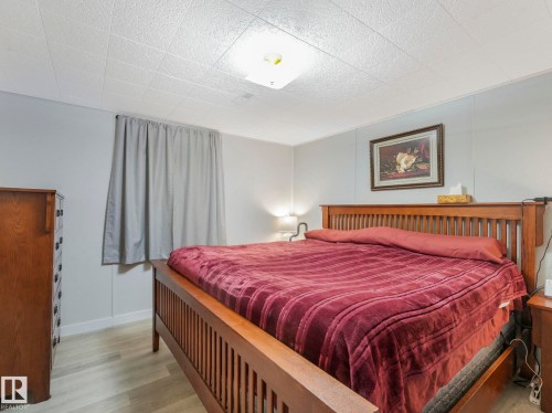 This room features light-colored plank flooring, a window with curtains, and a ceiling with textured panels and a central light fixture - 16106 79A Avenue Nw, Edmonton, AB - Indoor Photo Showing Bedroom