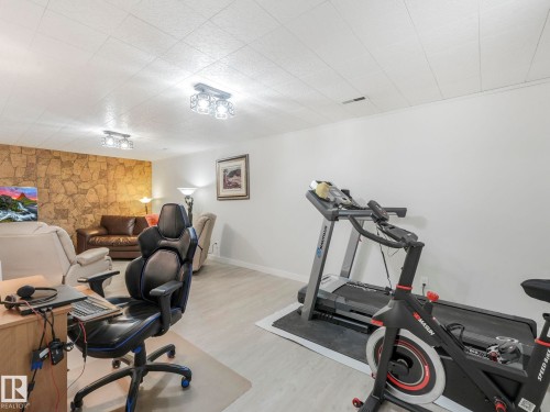 This versatile room features light-colored flooring, white walls, and a stone accent wall, providing distinct zones for various activities - 16106 79A Avenue Nw, Edmonton, AB - Indoor Photo Showing Gym Room