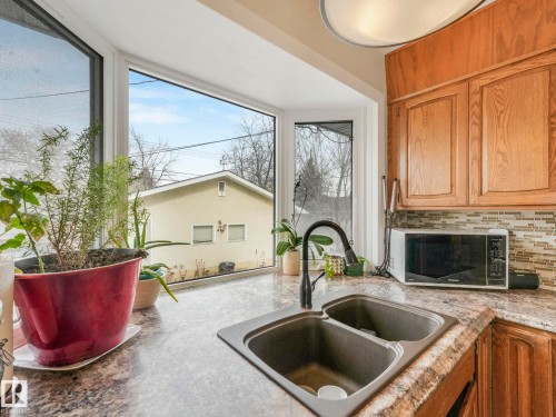 The kitchen features a double basin sink with a gooseneck faucet, a bay window, and wood cabinetry - 16106 79A Avenue Nw, Edmonton, AB - Indoor Photo Showing Kitchen With Double Sink