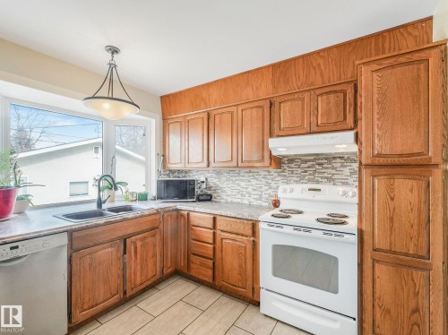 The kitchen features wood cabinetry, a tile backsplash, and a large window above the sink - 16106 79A Avenue Nw, Edmonton, AB - Indoor Photo Showing Kitchen With Double Sink