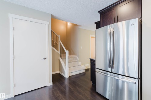 The property features dark wood flooring, a white door with a contemporary handle, a carpeted staircase with white railings, and a modern stainless steel refrigerator - 16811 120 Street, Edmonton, AB - Indoor