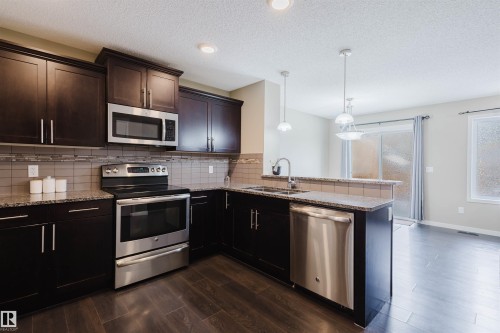 The kitchen features dark wood cabinetry, stainless steel appliances, granite countertops, and a tiled backsplash - 16811 120 Street, Edmonton, AB - Indoor Photo Showing Kitchen With Stainless Steel Kitchen With Double Sink With Upgraded Kitchen