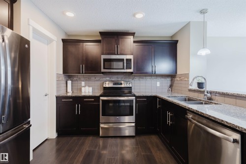 The kitchen features dark wood cabinetry, stainless steel appliances, granite countertops, and a tiled backsplash - 16811 120 Street, Edmonton, AB - Indoor Photo Showing Kitchen With Stainless Steel Kitchen With Double Sink With Upgraded Kitchen