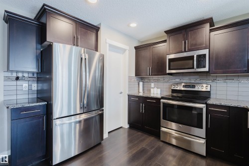 The kitchen features dark wood cabinetry, granite countertops, and stainless steel appliances including a refrigerator, range, and microwave - 16811 120 Street, Edmonton, AB - Indoor Photo Showing Kitchen With Stainless Steel Kitchen With Upgraded Kitchen