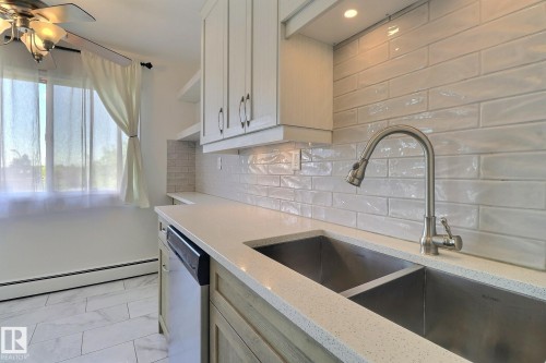 Kitchen with light stone counters, stainless steel dishwasher, baseboard heating, a ceiling fan, and light marble finish floors - 304 11907 81 Street, Edmonton, AB - Indoor Photo Showing Kitchen With Double Sink