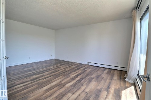 Empty room featuring dark wood-type flooring, a baseboard radiator, and a textured ceiling - 304 11907 81 Street, Edmonton, AB - Indoor Photo Showing Other Room