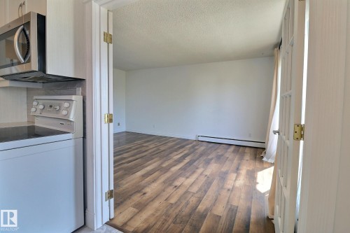Kitchen with white range with electric cooktop, stainless steel microwave, dark wood-style flooring, a textured ceiling, and a baseboard radiator - 304 11907 81 Street, Edmonton, AB - Indoor