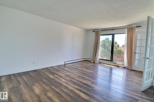 Spare room with dark wood-style flooring, a textured ceiling, and baseboard heating - 304 11907 81 Street, Edmonton, AB - Indoor Photo Showing Other Room