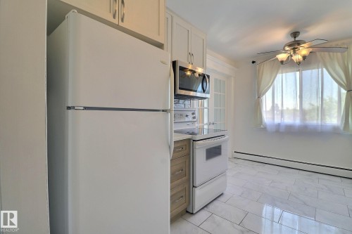Kitchen with white appliances, a baseboard radiator, ceiling fan, and light countertops - 304 11907 81 Street, Edmonton, AB - Indoor Photo Showing Kitchen