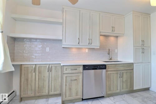 Kitchen featuring open shelves, stainless steel dishwasher, baseboard heating, tasteful backsplash, and light stone counters - 304 11907 81 Street, Edmonton, AB - Indoor Photo Showing Kitchen With Upgraded Kitchen