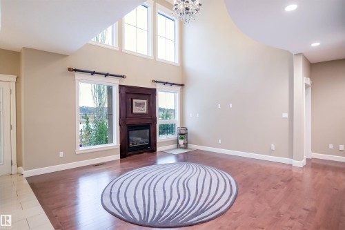 This living area features rich hardwood flooring, a striking corner fireplace with a dark wood surround, and high ceilings with upper windows that allow for ample natural light - 4016 Mactaggart Drive, Edmonton, AB - Indoor With Fireplace