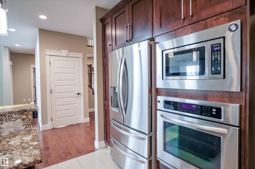 The kitchen features stainless steel appliances, including a microwave, oven, and refrigerator, integrated into dark wood cabinetry - 4016 Mactaggart Drive, Edmonton, AB - Indoor Photo Showing Kitchen