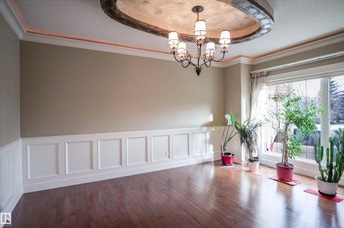 This room features hardwood flooring, white wainscoting, and a decorative ceiling with a chandelier - 4016 Mactaggart Drive, Edmonton, AB - Indoor Photo Showing Other Room