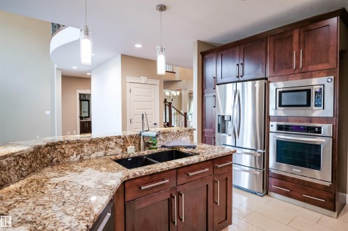 The kitchen features rich wood cabinetry, granite countertops, and stainless steel appliances, including a built-in oven, microwave, and refrigerator - 4016 Mactaggart Drive, Edmonton, AB - Indoor Photo Showing Kitchen With Double Sink With Upgraded Kitchen
