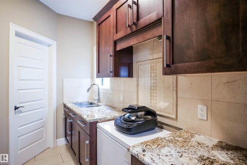 This functional space features dark wood cabinetry, granite countertops, and a stainless steel sink with a gooseneck faucet - 4016 Mactaggart Drive, Edmonton, AB - Indoor Photo Showing Kitchen With Double Sink