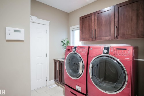This room features a pair of front-loading appliances, dark wood cabinetry, and tiled flooring - 4016 Mactaggart Drive, Edmonton, AB - Indoor Photo Showing Laundry Room