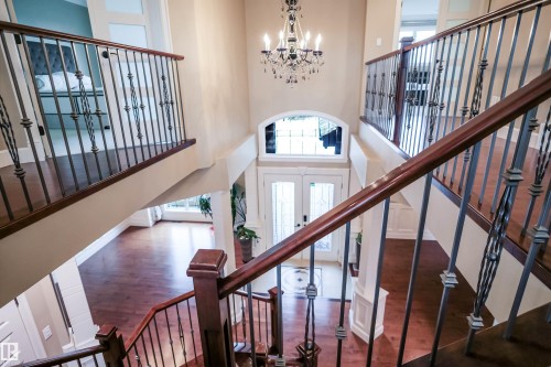 Grand entryway featuring a chandelier, a double front door with glass panels, and a staircase with decorative iron railings and hardwood treads - 4016 Mactaggart Drive, Edmonton, AB - Indoor Photo Showing Other Room
