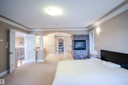 Spacious room featuring carpeted flooring, a stone-accented fireplace, and a large window providing natural light - 4016 Mactaggart Drive, Edmonton, AB - Indoor Photo Showing Bedroom