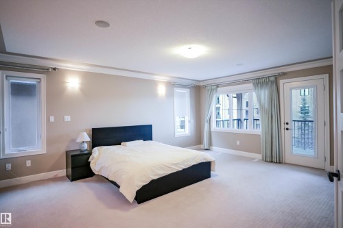 This inviting room features a spacious layout with light-colored carpeting, windows that provide natural illumination, and a door leading to a balcony - 4016 Mactaggart Drive, Edmonton, AB - Indoor Photo Showing Bedroom